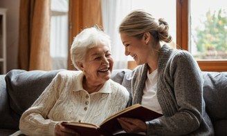 Eine Helferin und eine Seniorin sitzen lächelnd beieinander