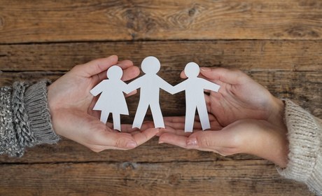 Zwei Hände halten behutsam eine Familie aus Papierfiguren